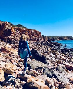 Rear view of girl walking on rocks at beach against sky