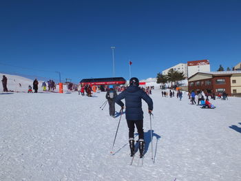 People skiing on snowcapped landscape against clear blue sky