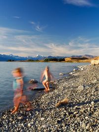 Blurred motion of boys playing at beach against sky