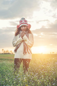 Woman in warm clothing standing on field against cloudy sky