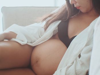 Midsection of pregnant woman relaxing on sofa at home