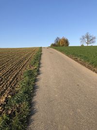 Road amidst field against clear sky