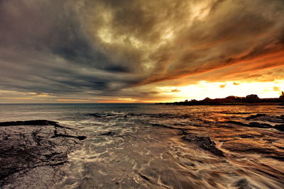 Scenic view of sea against dramatic sky during sunset