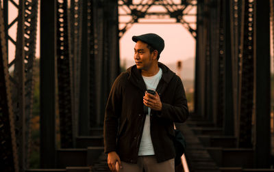 Young man looking away while standing against wall