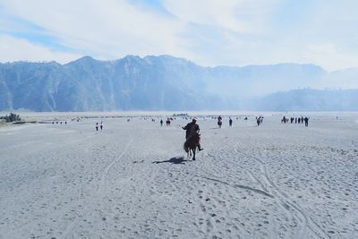 Man riding horse on sand in desert against sky