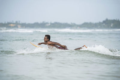 Shirtless man surfing in sea against sky