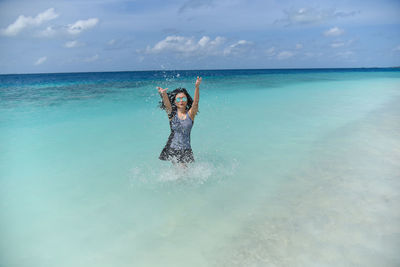 Portrait of young woman standing in sea against sky