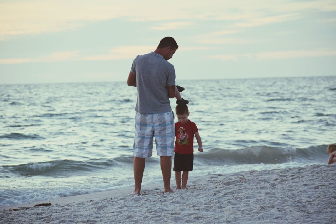 sea, water, horizon over water, rear view, lifestyles, sky, beach, full length, leisure activity, standing, wave, men, shore, scenics, beauty in nature, vacations, tranquil scene, casual clothing