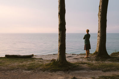 Rear view of woman standing by sea against sky