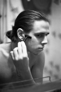 Shirtless young man shaving reflecting on mirror in bathroom at home