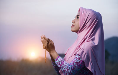 Side view of woman wearing hat against sky during sunset