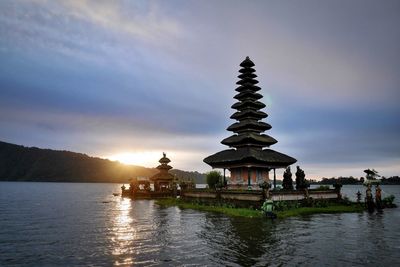 Traditional building by lake against sky during sunset
