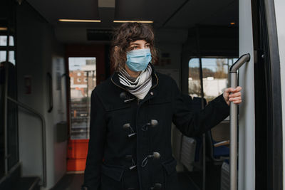 Woman wearing mask standing by train on railroad station platform