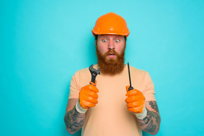 Portrait of young man wearing hat standing against blue background