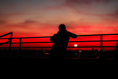 Silhouette of man standing by railing against sky during sunset