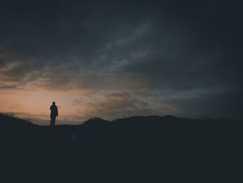 Silhouette person standing on land against sky during sunset
