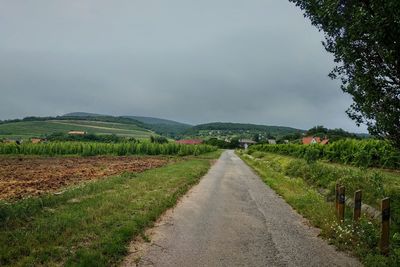 Empty road amidst field against sky