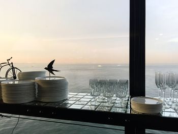 Plates stacked by glasses on table against sky during sunset