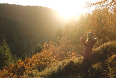 Woman photographing trees through mobile phone