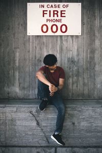 Full length of man sitting against wall