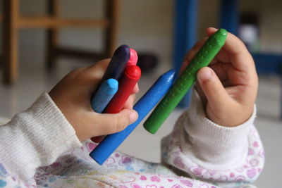 Midsection of child holding colorful crayons while lying at home