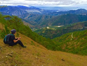 Side view of hiker sitting by mountains against sky