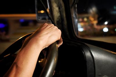 Cropped hand of man driving car at night
