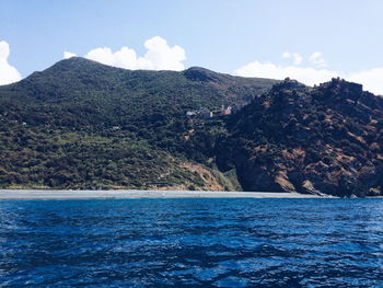 Scenic view of sea by mountain against sky