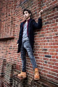 Full length of young woman standing against brick wall