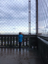 Rear view of teenage boy looking through coin-operated binoculars at observation point in city