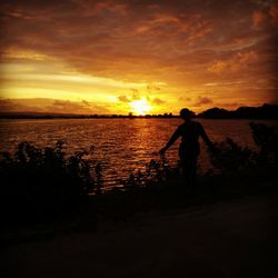 Silhouette man standing by sea against sky during sunset