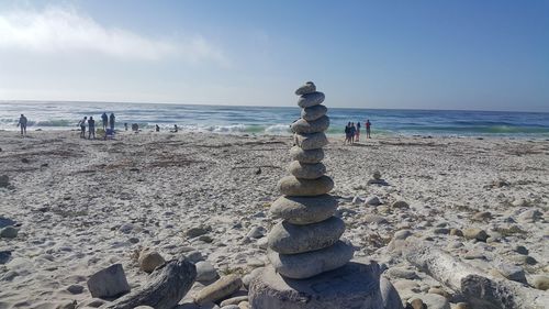 Stack of pebbles on sand at beach against sky