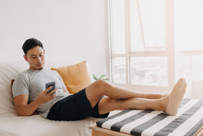 Young man using laptop while sitting on bed at home