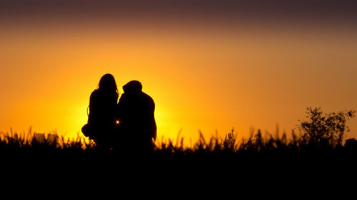 Silhouette couple on field against sky during sunset