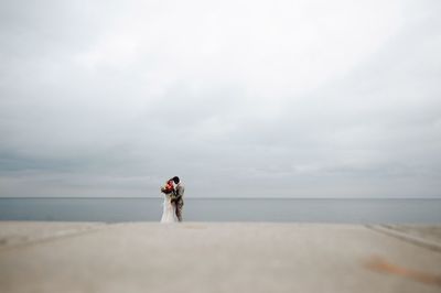 Bride and bridegroom standing on pier in sea during wedding ceremony