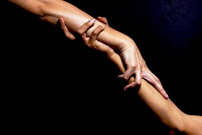 Cropped image of women with holding hands against black background