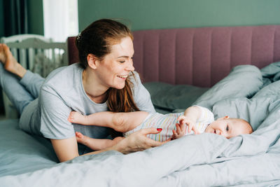 Young mom has fun playing with the baby in bed. a caring mom is raising a newborn daughter.