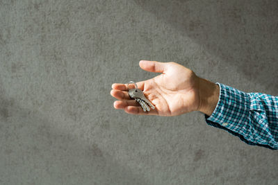 Close-up of man holding key against wall