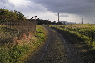 Empty road amidst field against sky