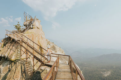 Woman standing on footbridge over mountain during foggy weather