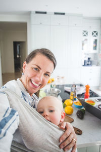 Portrait of smiling food blogger carrying daughter in kitchen at home