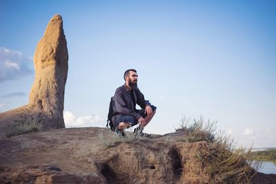 Man sitting on rock against clear sky