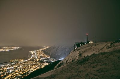 Aerial view of illuminated city by mountain against sky during winter