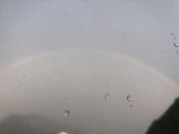 Close-up of raindrops on window against sky