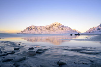 Scenic view of sea and snowcapped mountains against clear sky during sunset