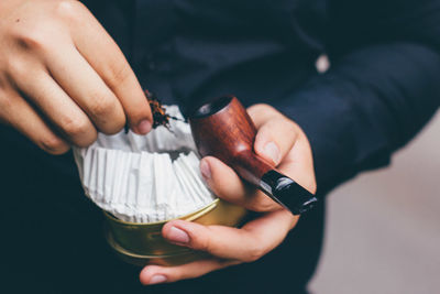 Midsection of man holding smoking pipe