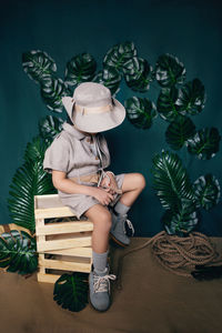 Boy child traveler in a hat sits on wooden boxes in a studio on a green background