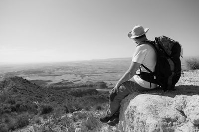 Side view of man sitting on rock against sky