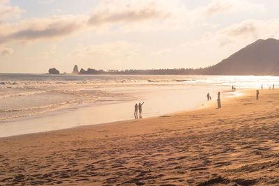 People at beach against sky during sunset