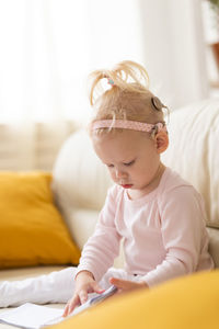 Portrait of cute baby girl sitting on bed at home